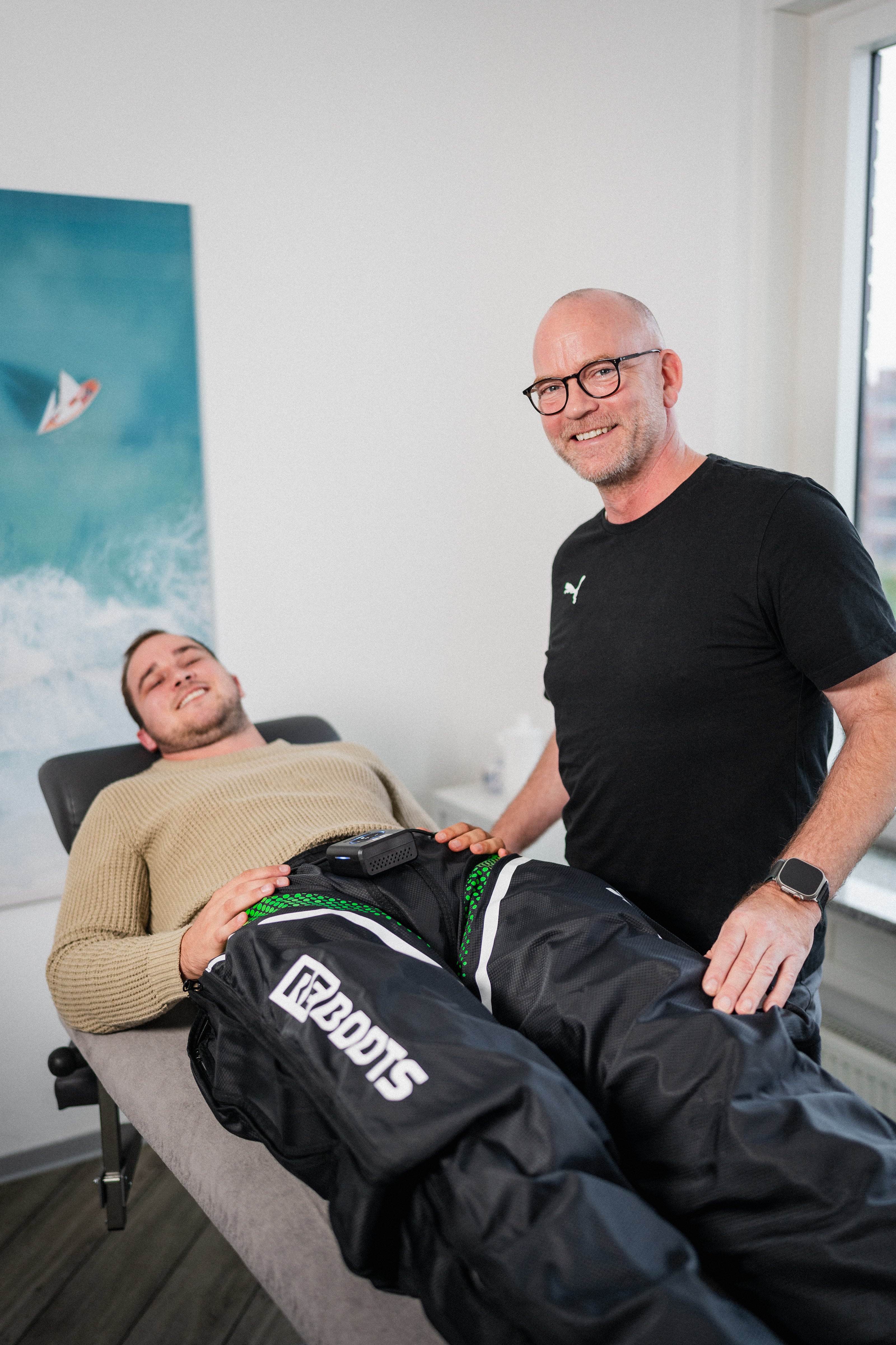 Dr. Philip Lübke, Facharzt für Orthopädie und Reboots Experte, betreut einen Patienten bei der Kompressionsmassage mit dem Reboots Go X in seiner Praxis in Kiel.