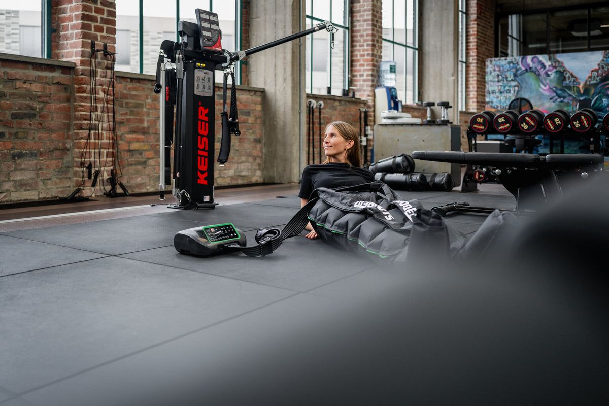 Athletin entspannt mit Reboots Kompressionsmassage-Gerät, dem Reboots One Lite, im Gym zur schnelleren Muskelregeneration.