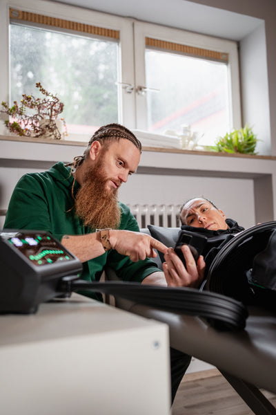 Physiotherapeut erklärt einer Patientin die Anwendung der Reboots One Pro Recovery Boots während einer Session.