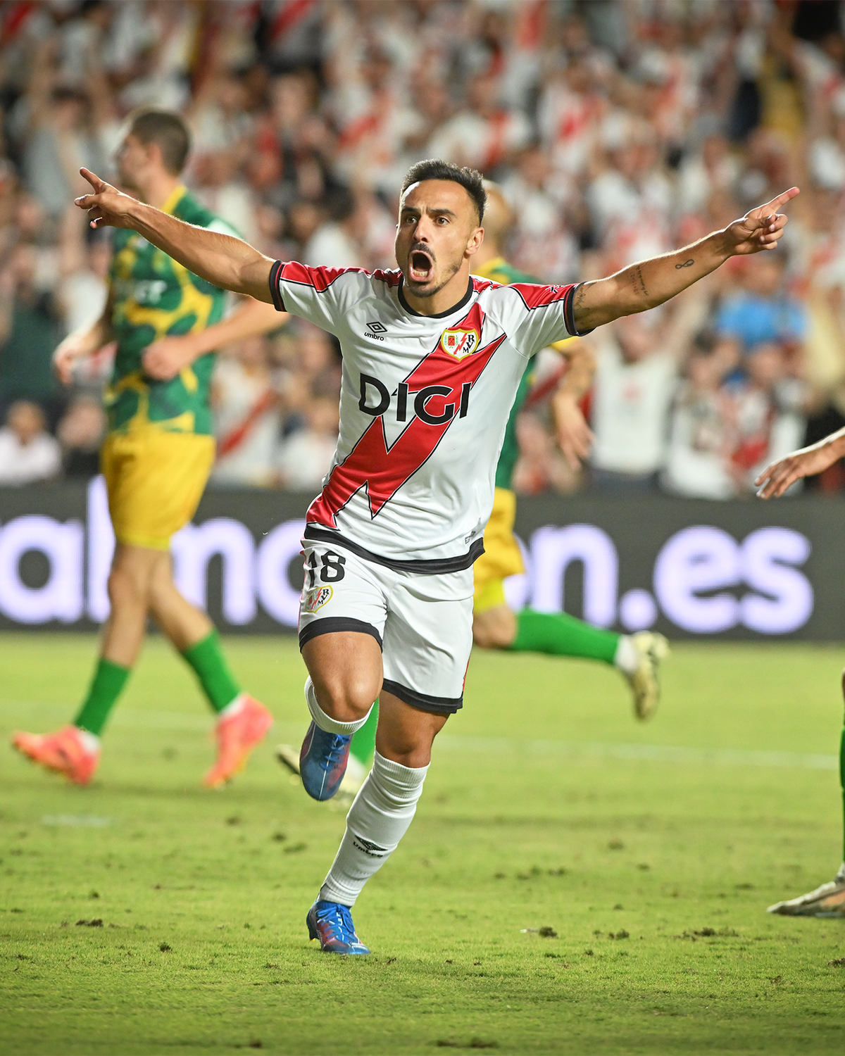 Fußballspieler von Rayo Vallecano jubelt nach einem Tor während eines Ligaspiels; dynamische Szene vor jubelnden Fans.