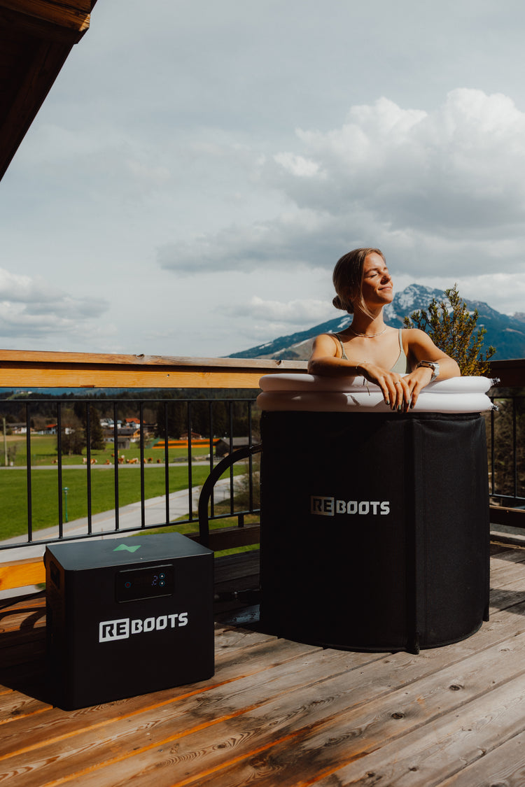 Reboots Ice Tub mit Chiller auf Terrasse – Frau entspannt im Eisbad mit Bergblick, moderne Kältetherapie für Regeneration und Recovery im Outdoor-Bereich-