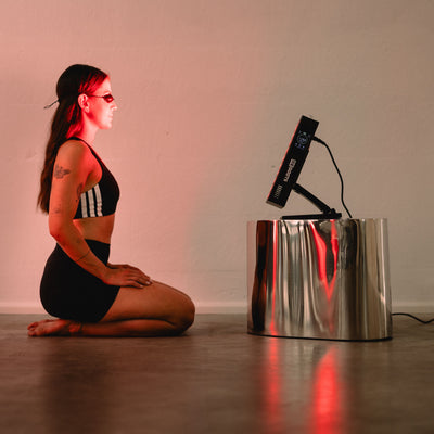 Frau kniet mit Schutzbrille vor dem Reboots Relight Mini Rotlichtpanel