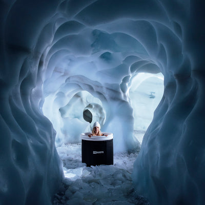 Sportlerin nutzt eine Reboots Eisbad-Tonne für Kältetherapie zur Regeneration in einer natürlichen Eishöhle.