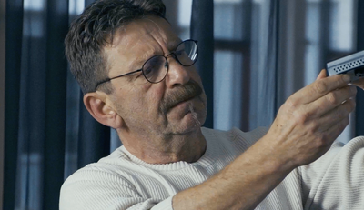 Älterer Mann mit Brille betrachtet und prüft ein kleines elektronisches Gerät in den Händen