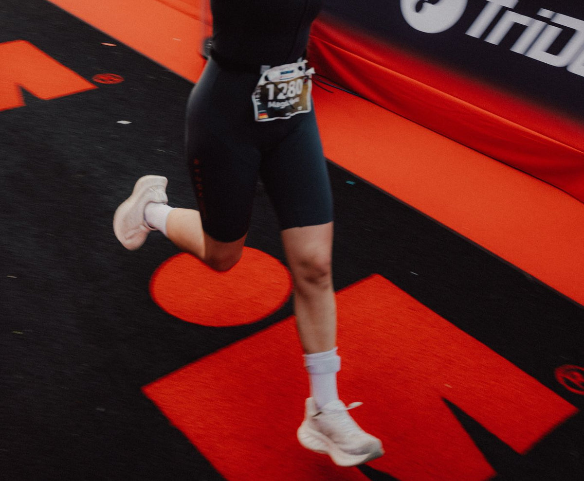 Triathletin läuft unter Applaus der Zuschauer über den roten Teppich ins Ziel eines IRONMAN Triathlons.