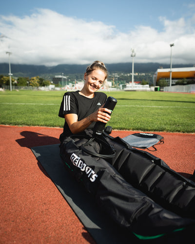 Sportlerin nutzt Reboots Recovery Boots zur Regeneration nach dem Training auf der Laufbahn – mobile Kompressionsmassage für schnellere Erholung und bessere Performance.